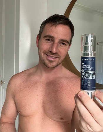 Man holding Particle Men's Formula Face Cream bottle.