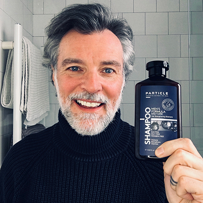 Middle-aged man holds a Particle shampoo bottle and smiles.