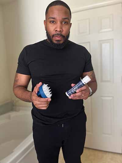 Man in black clothes holding Particle hair care products in a bathroom.