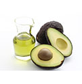 Avocado halves and oil in a glass jug on a white background.