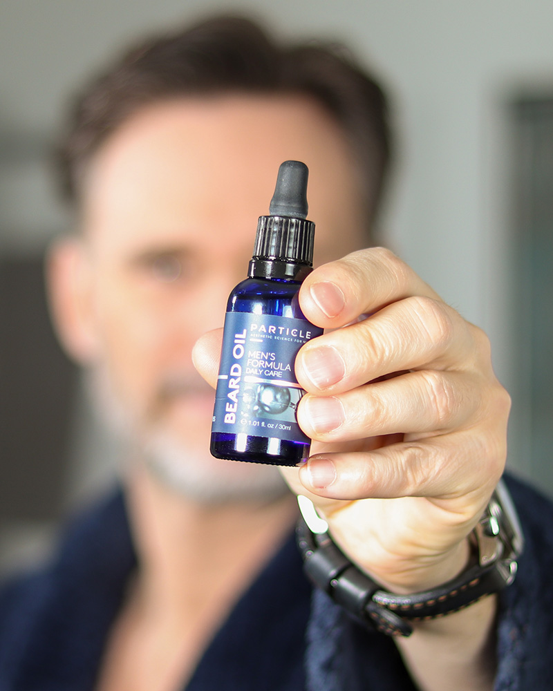 Man holding a small bottle of a Particle Beard Oil Men's Formula Daily Care.