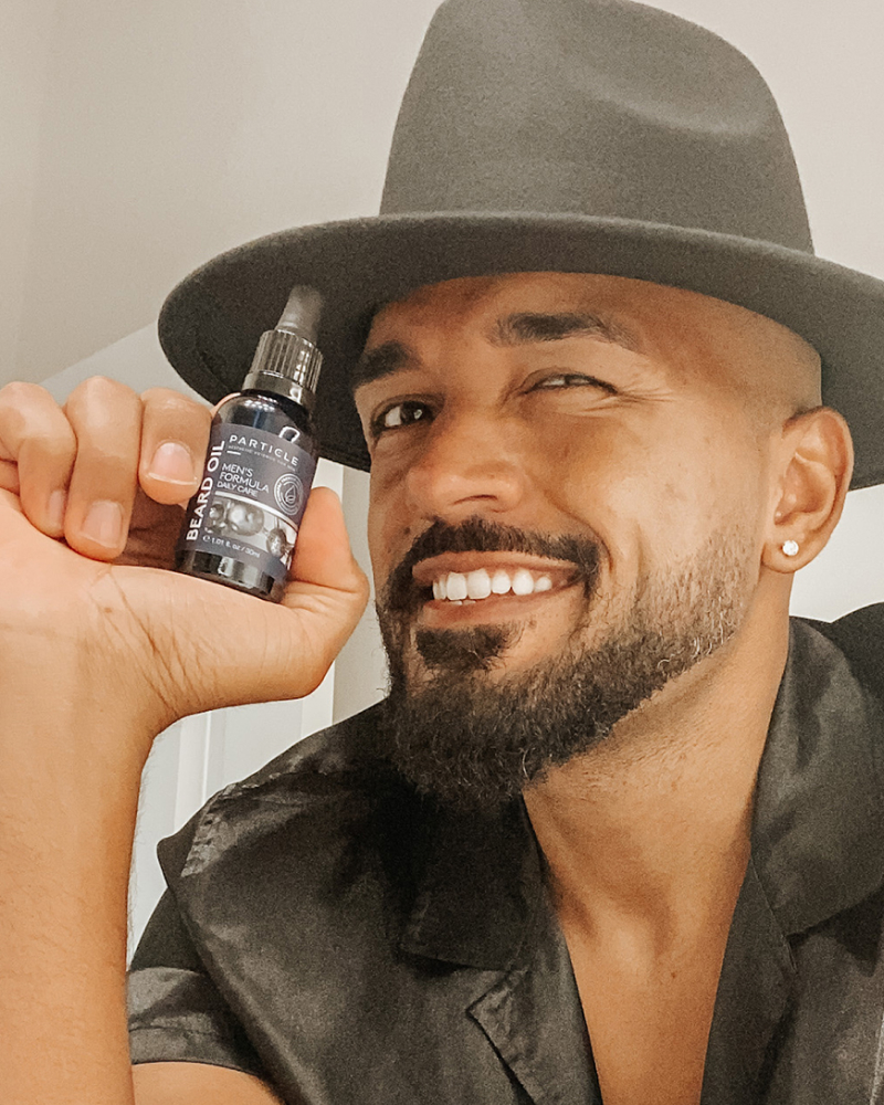 Man holding a bottle of Particle Beard Oil, smiling and winking.