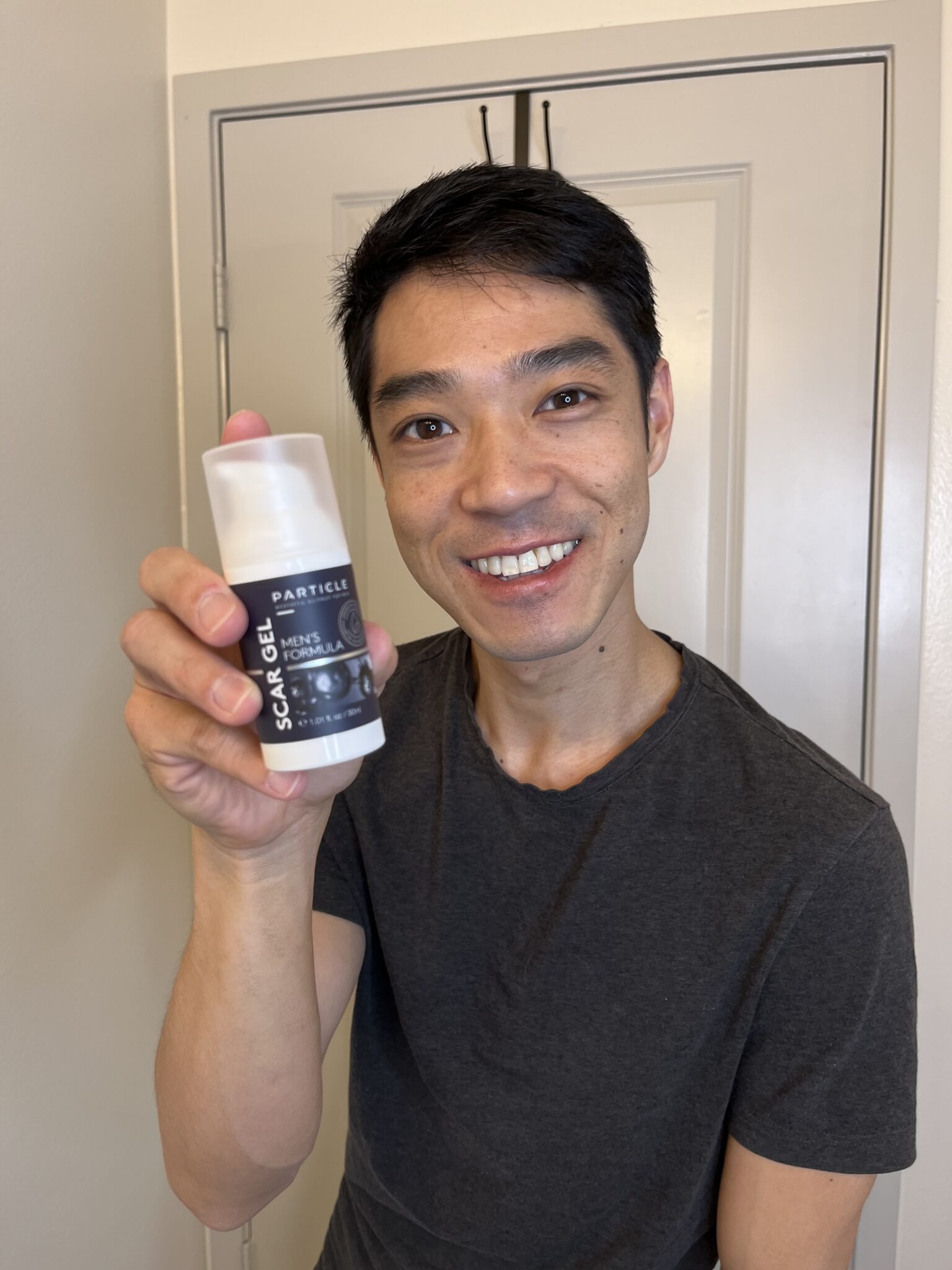 Man smiling, holding Particle Scar Gel Men's Formula box.