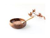 Wooden bowl contains brown powder, spoon, and dry twig.