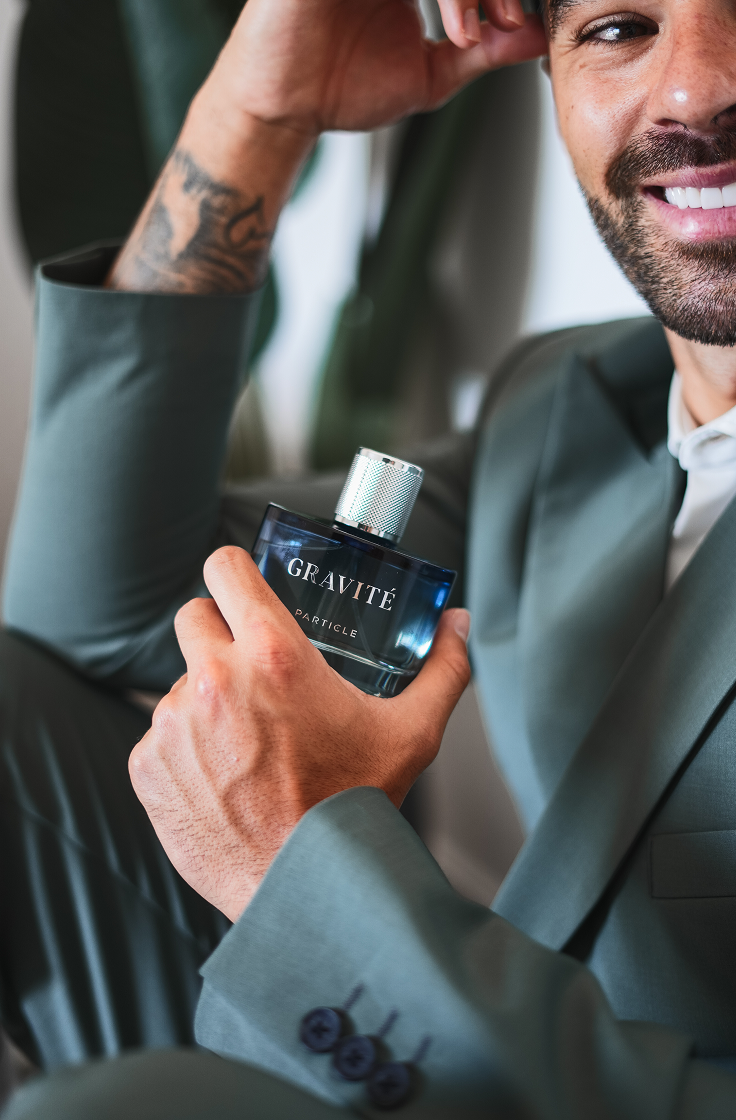 Smiling man holding Gravité men’s perfume bottle, showcasing a confident and stylish masculine fragrance