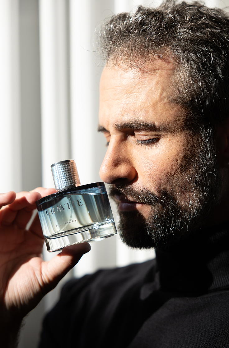 Man smelling Gravité men’s perfume bottle, capturing a sophisticated and contemplative masculine fragrance moment
