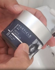 Hands holding a Particle Men's Formula face cream jar with silver lid in a bathroom